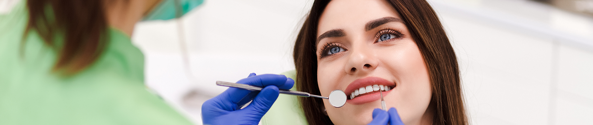 A person is seated in a dental chair, receiving care from a dental professional who stands behind them.